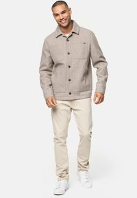 Veste en laine gris clair avec un col, poches poitrine et boutons noirs, assortie à un pantalon beige et des baskets blanches.