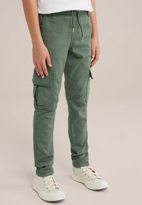 Gröna cargobyxor med elastisk midja, flera sidofickor och en tapered passform, samt vita låga sneakers.