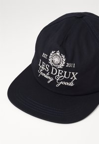 Navy blue cap with a curved brim. Features white embroidered text, including "LES DEUX" and a decorative emblem. Text includes a year, 2011.