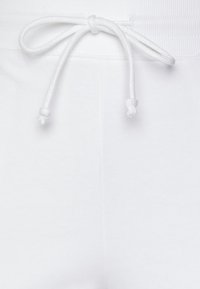 Vita sweatpants med ribbad midja och snöre med knut, slät textur och inga synliga mönster eller grafiska detaljer.