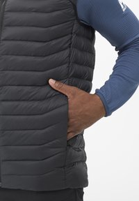 Gilet noir rembourré avec un motif en chevrons et une poche latérale, associé à une chemise à manches longues bleue en tissu texturé.