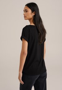 Must have lühikeste varrukatega must T-särk, millel on rullitud varrukad, tekstuuriga laineline muster, lõdva lõikega ja siledast kangast.