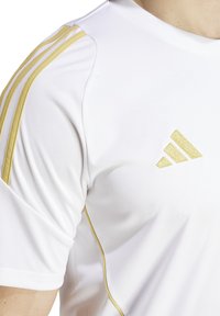 Witte sportshirt met gouden accenten op de schouders, voorzien van drie gouden strepen en een klein gouden merklogo op de borst.
