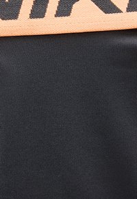 Κοντινή λήψη σκούρου γκρι υφάσματος με ραβδώσεις, με πορτοκαλί ταινία που φέρει μαύρες διαγώνιες ρίγες κατά μήκος της πάνω άκρης.