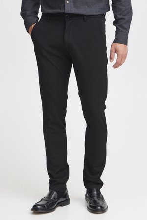 Pantaloni negri, ajustați pe corp, cu o textură netedă, având închidere cu nasture și buzunare. Asortați cu mocasini negri și o cămașă gri cu nasturi.