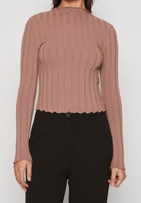 Long-sleeve ribbed top, mauve color, featuring a scalloped neckline and hem, made of textured fabric, paired with black high-waisted trousers.