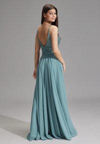 Abito da sera teal con schiena a V profonda, corpetto impreziosito e gonna fluente. Presenta spalline sottili e una superficie liscia.