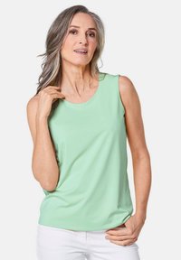 Lichtgroene mouwloze top gemaakt van een gladde stof, met een ronde halslijn en een ontspannen pasvorm. Draag het met witte broeken.