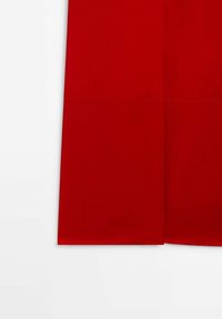 Partie inférieure d'un vêtement rouge avec un ourlet droit et un détail de couture horizontale, sur fond blanc.