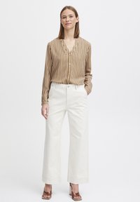 Brown and white striped blouse with a v-neck, button front; paired with high-waisted, wide-leg white pants and brown heeled sandals.