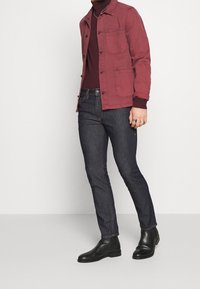 Burgundy stofjacka med två bröstfickor, kombinerad med mörkblå slim-fit jeans och svarta läder anklar stövlar.