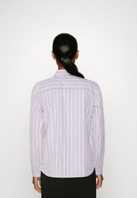 Langearm shirt met verticale blauwe en rode strepen op een witte achtergrond; heeft een klassieke kraag en een afgeronde zoom.