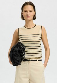 Beige sleeveless top with black horizontal stripes, round neckline, paired with light-colored trousers and a black crochet bag.