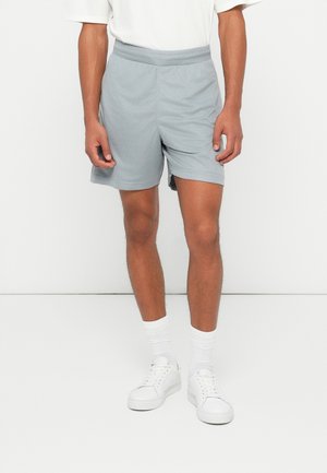 Ljust grå träningsshorts med elastiskt midjeband, normal passform och något strukturerad tyg, ihop med vita sneakers och strumpor.