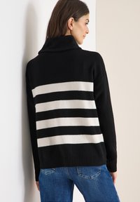 Pull à rayures noir et blanc avec un col montant, un ourlet côtelé et une texture tricotée confortable, associé à un jean en denim bleu.