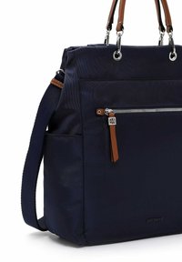 Marineblå mulepose med lomme med lynlås foran, brun læderlynlås, håndtag, justerbar skulderrem og EMILY & NOAH-logo.