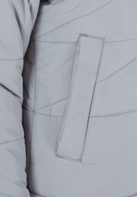 Secțiune de jachetă puffer gri cu o suprafață texturată, având cusături diagonale și un buzunar tip patch pe partea stângă.