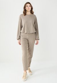Beżowy zestaw odzieży domowej z dzianiny, składający się z luźnej bluzki z okrągłym dekoltem oraz dopasowanych spodni. Połączony z jasnymi sneakersami.
