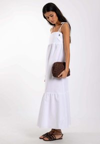 Vestido maxi blanco sin mangas con un dobladillo en capas y tejido texturizado, combinado con un bolso de mano marrón texturizado y sandalias negras de tiras.