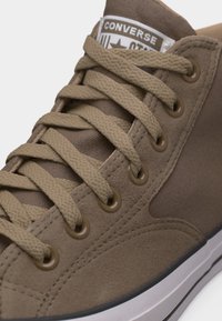 Smeđa Converse tenisica s teksturiranim vezicama, metalnim ulićama i bijelim gumenim đonom, na jeziku je prikazan logotip brenda.