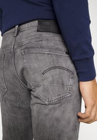 Grå denimjeans med en falmet finish, med en svart skinnbelteetikett, to baklommer og subtile broderidetaljer.