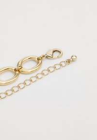 Bracelet en tons dorés avec des maillons ovales, une section de chaîne, et un fermoir en forme de homard. Texture lisse avec une finition brillante et une petite balle décorative.