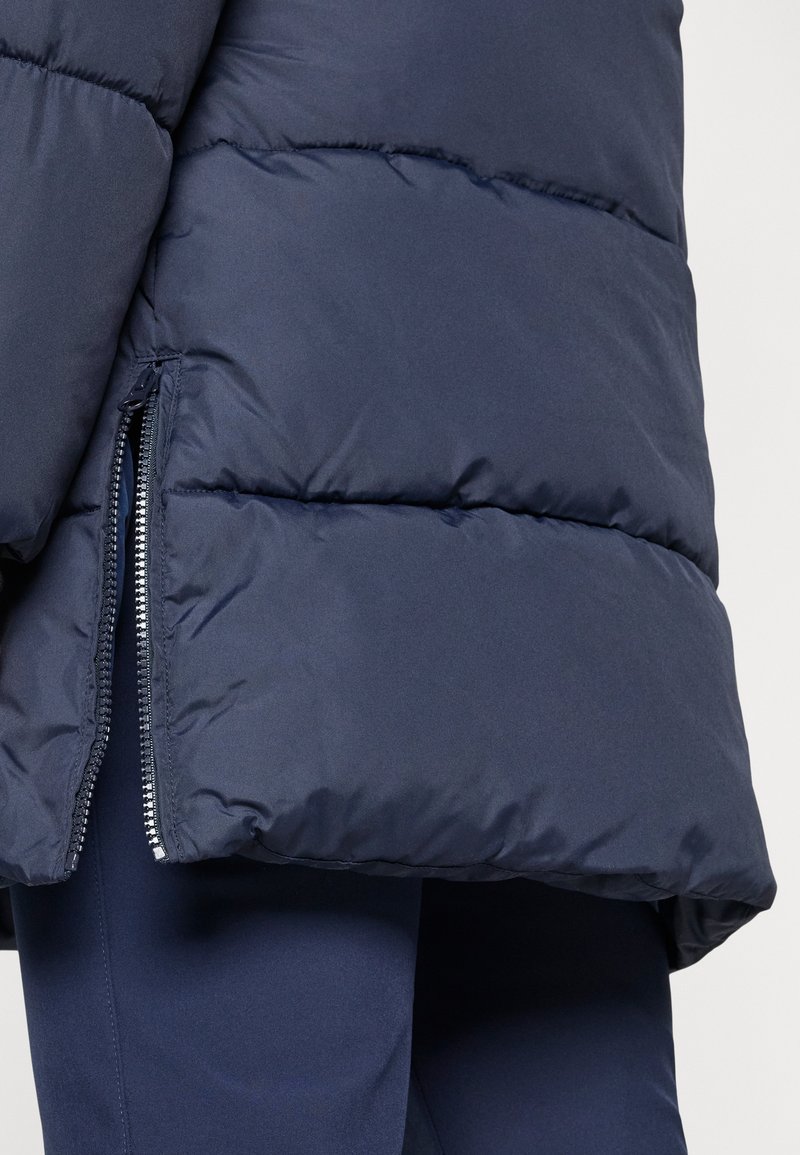 Veste doudoune bleu marine foncé avec des sections matelassées, une texture lisse et une fermeture éclair sur le côté.