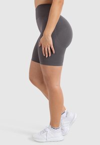 Graue, hochtaillierte Shorts mit glatter Textur, die einen figurbetonten Schnitt haben und bis zur Mitte des Oberschenkels reichen, kombiniert mit weißen Sportschuhen.