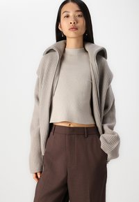 Pull court côtelé beige avec un motif en V et un cardigan oversize gris clair. Associez-le à un pantalon tailleur marron taille haute.