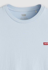 Světle modré bavlněné tričko s kulatým výstřihem a krátkými rukávy. Obsahuje malé červené vyšívané logo Levi's na levé části hrudi.