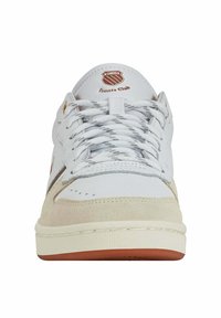 Zapatilla blanca con puntera de gamuza y acentos grises. Detalles metálicos dorados en el lateral, con una suela de goma texturizada y logo en la lengua.