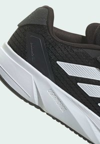 Zapatilla deportiva negra con un upper texturizado, acentos de franja blanca y una suela de goma en contraste. El diseño incluye un collar acolchado y un logotipo.