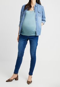 Maternity outfit featuring a light blue tank top, denim shirt, dark blue skinny jeans, and leopard print flats. Casual and comfortable fit.