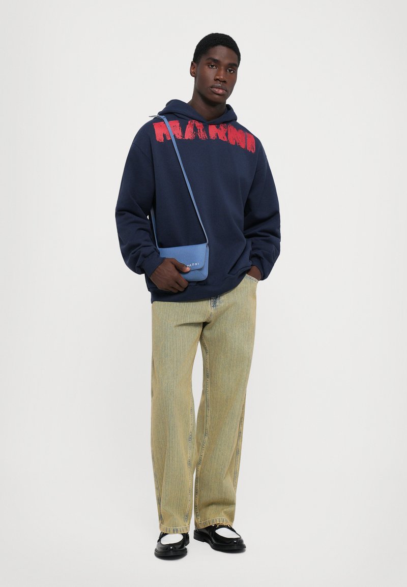 Navy hoodie with red graphic, light striped wide-leg pants, black shoes, and blue crossbody bag. Simple, casual streetwear outfit.
