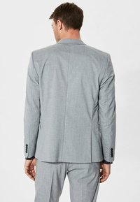 Chaqueta de traje gris claro con solapas de muesca, abertura simple y puños de tres botones. Textura suave y ajuste entallado. Vista posterior mostrada.