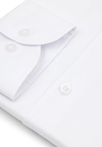 Białą koszulę z mankietami złożonymi z dwiema perłowymi guzikami, wyeksponowaną na tle białej tkaniny.