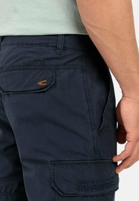 Marine cargo shorts zijn gemaakt van een gestructureerde stof, hebben platte zakken en een geborduurde "MADE FOR ADVENTURES" detail. Oranje logo accent op de zak.