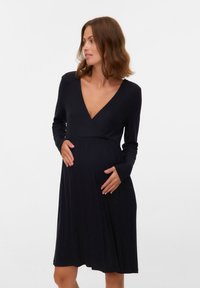 Czarna prążkowana sukienka ciążowa z długimi rękawami, głębokim dekoltem w serek i sylwetką w kształcie litery A, wykonana z miękkiego materiału, z luźną spódnicą.