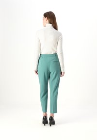 Maglione a collo alto in lana color crema, abbinato a pantaloni su misura color teal chiaro con tasche laterali e scarpe col tacco nere.