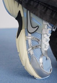 Nike sporta kurpes ar gaismas zilā un sudraba audumu, baltām stīgām un teksturētu krēmkrāsas zoli. Ievērojami sudraba akcenti sānos.