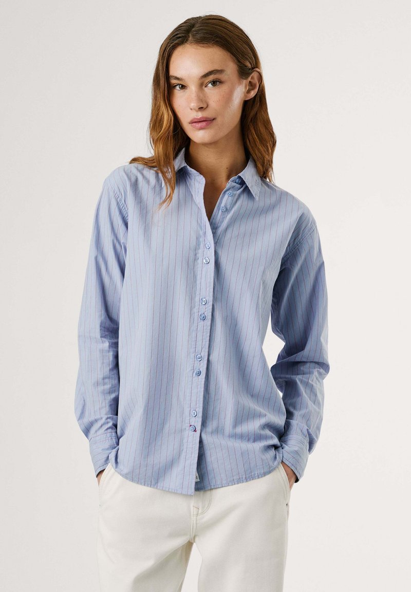 Chemise boutonnée bleu clair avec des rayures rouges verticales, à manches longues et col classique. Texture douce avec une coupe décontractée.