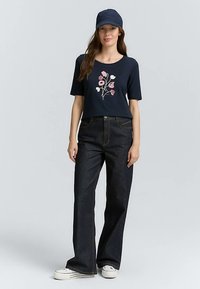 Navy short-sleeve t-shirt with floral embroidery on the front, paired with high-waisted dark denim jeans and white sneakers.
