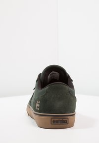 Adidași de skate din suede verde cu un guler din textil negru. Au o talpă din cauciuc bej și un logo proeminent pe toc. Design curat.
