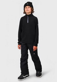 Μαύρη φλις μπλούζα με φερμουάρ και μακριά μανίκια, σε συνδυασμό με μαύρο cargo παντελόνι. Το φλις είναι απαλό και το παντελόνι έχει τσέπες. Ένα μαύρο καπέλο beanie και αθλητικά παπούτσια ολοκληρώνουν την εμφάνιση.