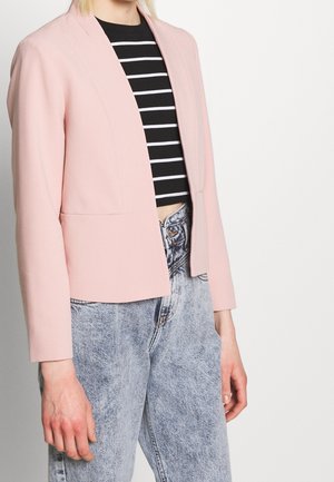 Personne portant un blazer rose clair sur un crop top rayé noir et blanc avec un jean taille haute bleu clair délavé à l'acide.