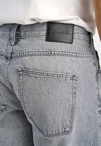 Szare dżinsy z denimu o fakturowanym wykończeniu. Posiadają czarną skórzaną naszywkę z logo na pasku w talii oraz dwie tylne kieszenie.