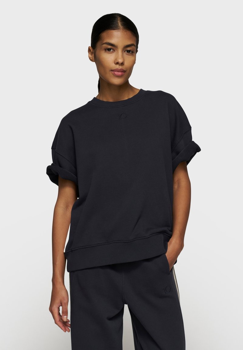 Mørkeblå oversized sweatshirt med oprullede manchetter, der har en diskret logo-detalje på brystet og ribbet kant. Blød stoftekstur.