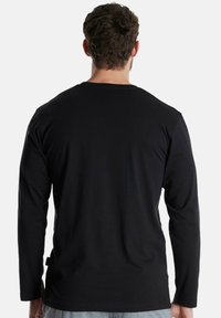 Camiseta de manga larga de color negro fabricada con tela suave, con cuello redondo, textura lisa y diseño liso en la parte trasera.