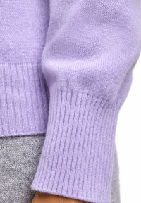 Cuff di maglione lavorato a maglia colore lavanda con texture a coste, abbinato a un tessuto grigio chiaro sottostante, che mostra un design pulito e senza soluzione di continuità.