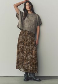 Šedý zkrácený svetr, plisovaná maxi sukně s hnědým leopardím potiskem a černé kotníkové boty s přezkami. Texturovaný pletený materiál, splývavá látka.